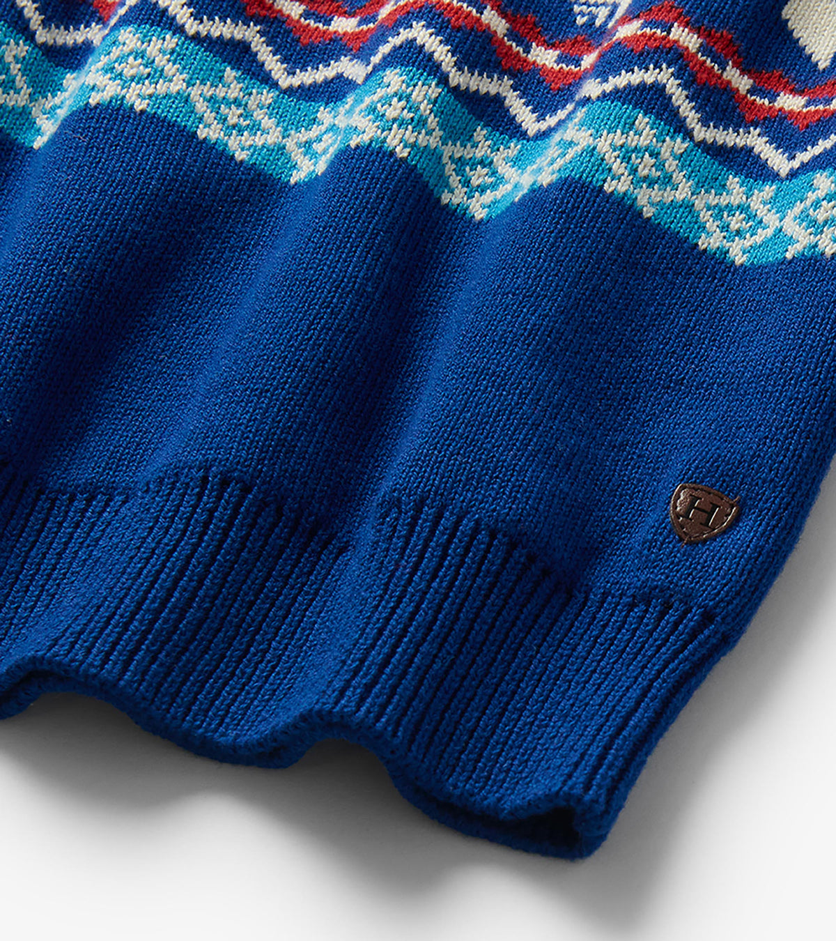 Close-up of blue sweater hem with ribbed trim, Fair Isle pattern, and small shield logo patch
