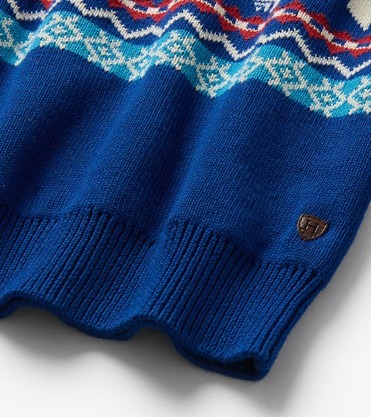Close-up of blue sweater hem with ribbed trim, Fair Isle pattern, and small shield logo patch