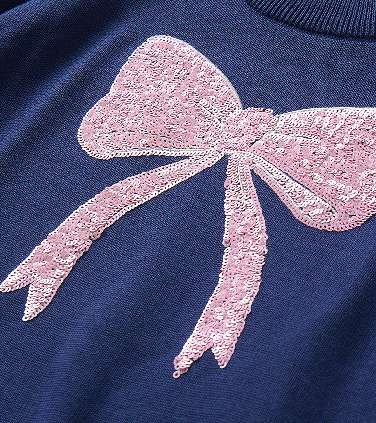 Close-up of pink sequin bow detail on the front of the navy sweater