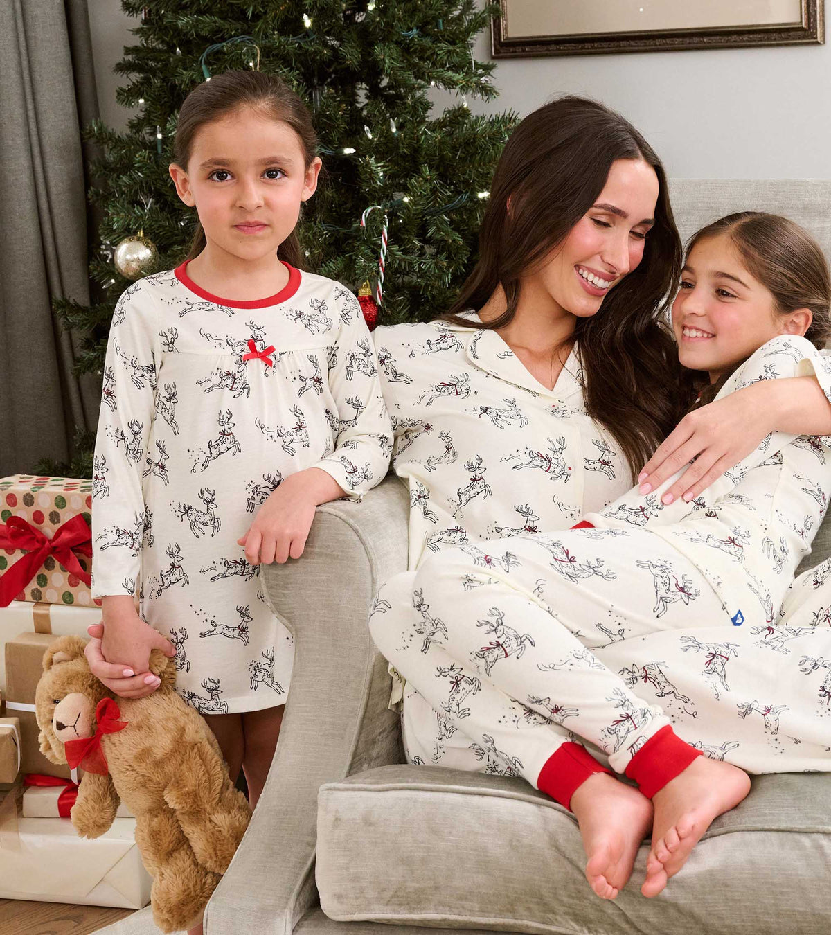 Girl wearing white reindeer print nightdress with red trim, standing by family in matching holiday pajamas