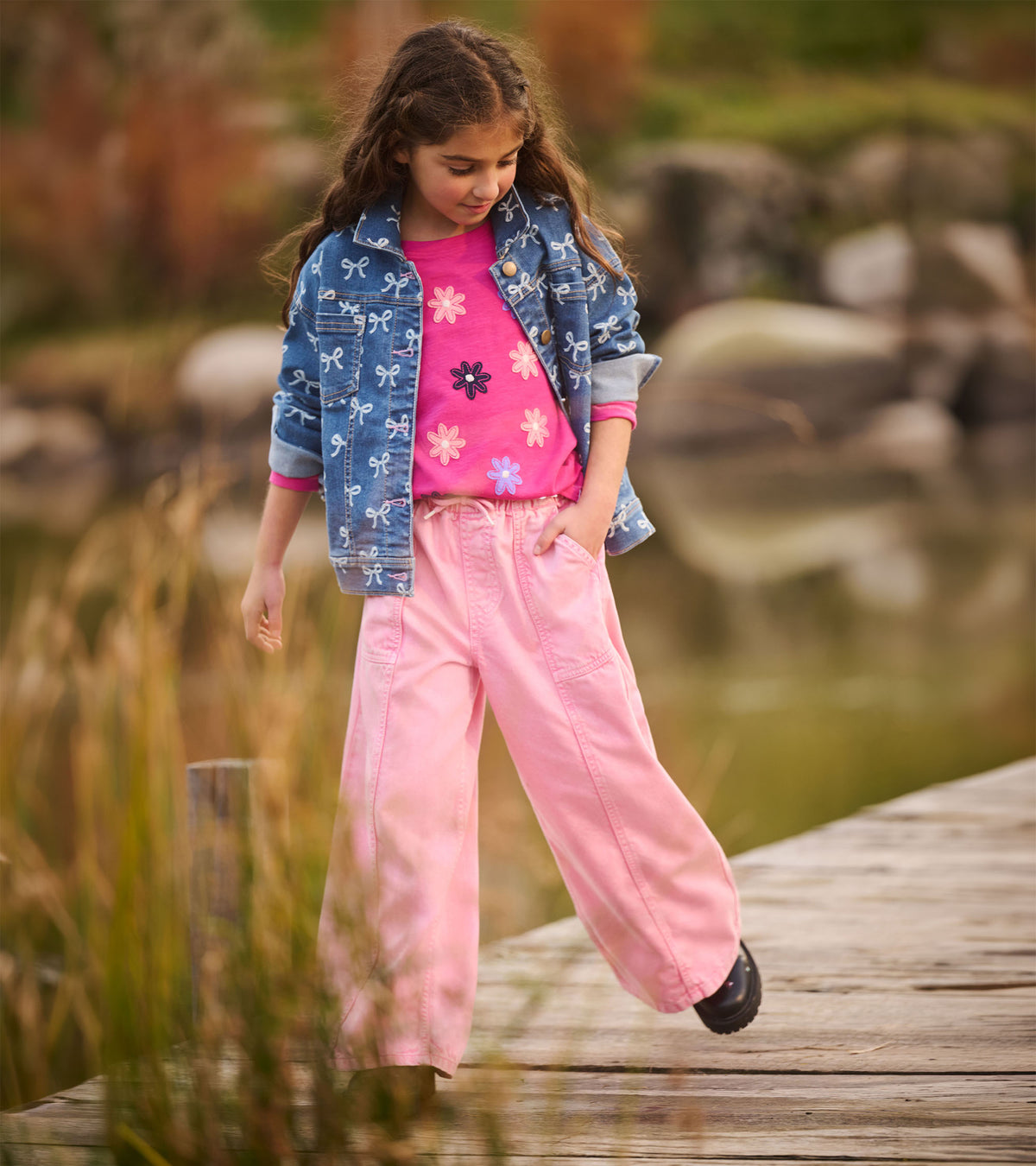 Girl wearing berry pink flower graphic T-shirt with a blue bow-print jacket and light pink pants