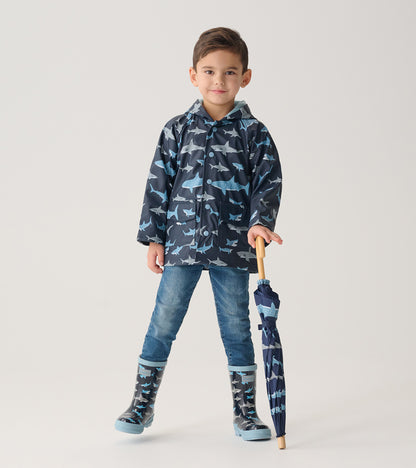Child modeling navy shark print raincoat with matching rain boots, holding a closed umbrella