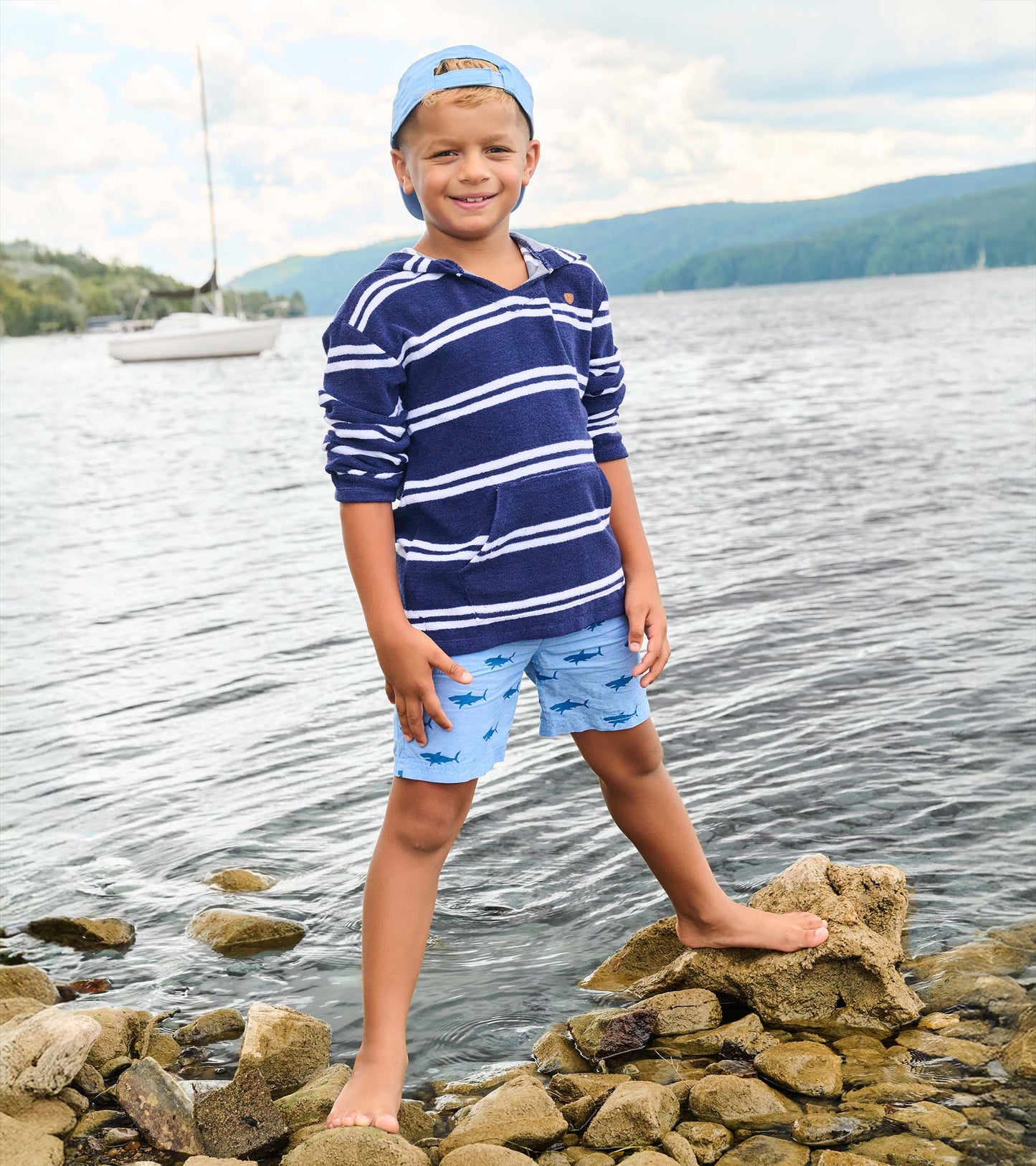 Light blue boys shorts with dark shark print, shown on a child standing on rocks by the water