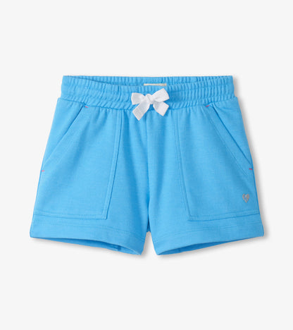Light blue girls shorts with elastic waist, white bow, front pockets, and small heart logo.