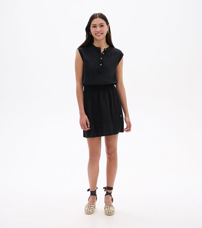 Black sleeveless dress with a buttoned neckline and elastic waist, styled with espadrille sandals.