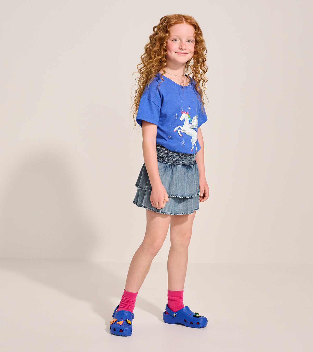 Girl wearing a light blue smocked denim tiered skirt, front view