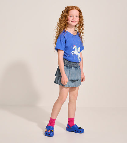 Girl wearing a light blue smocked denim tiered skirt, front view