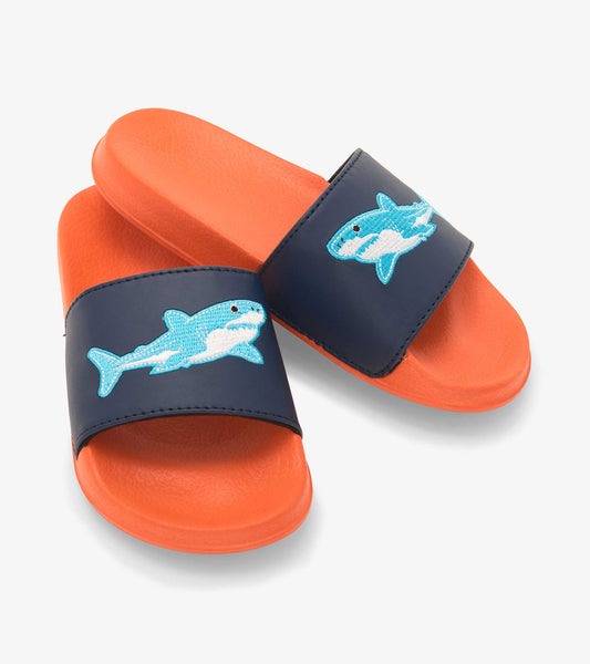 Navy slide sandals with orange soles, featuring a blue shark design on the strap. Suitable for kids.
