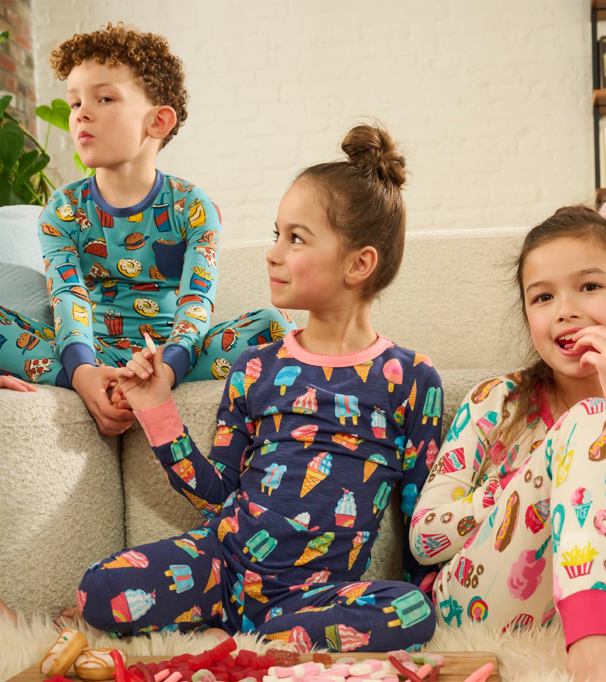 Children wearing colorful ice cream print long-sleeve pajama sets, seated indoors on a couch.