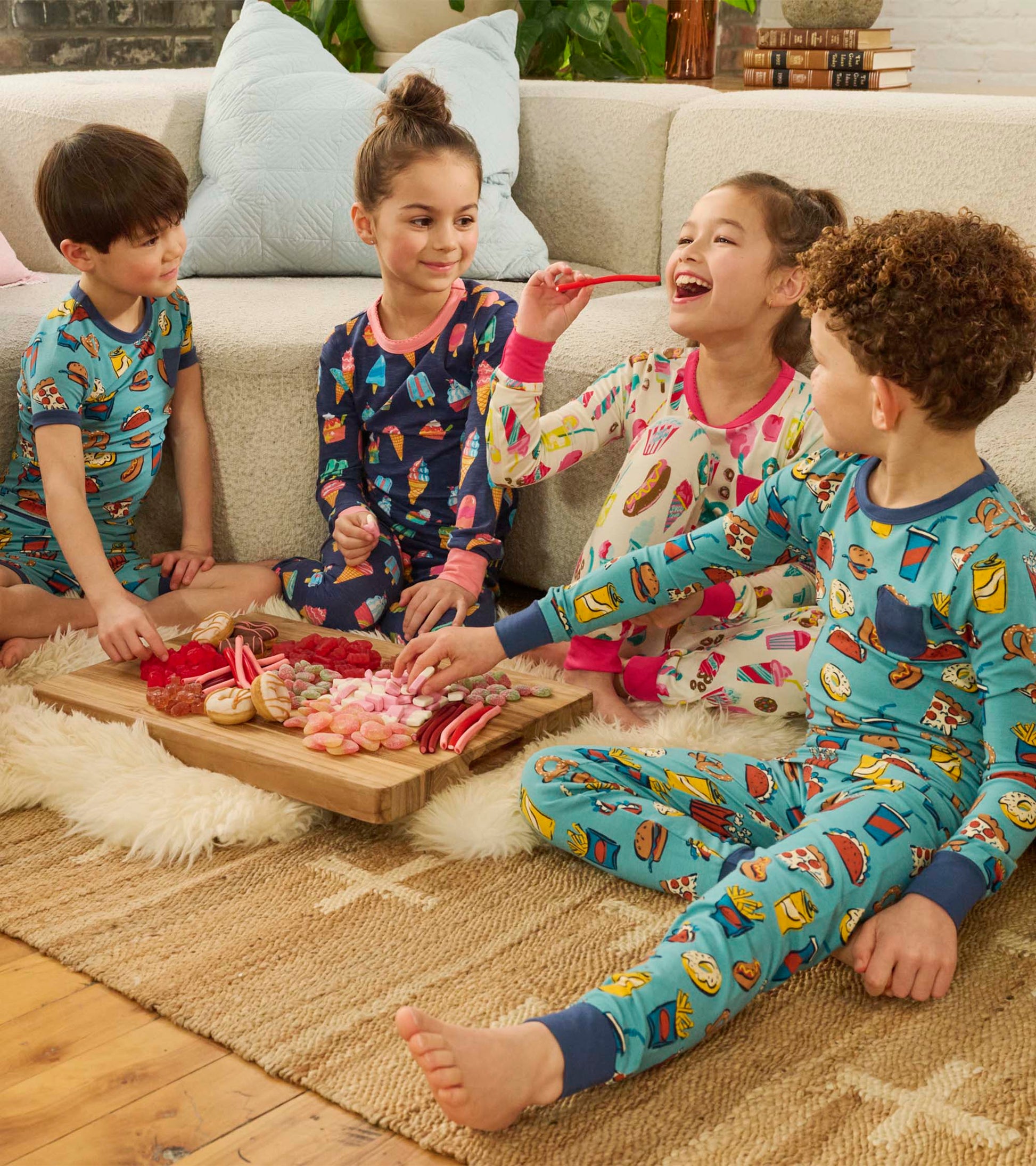 Colorful pyjama set featuring ice cream and treat patterns, worn by kids sitting on a rug with a snack platter.