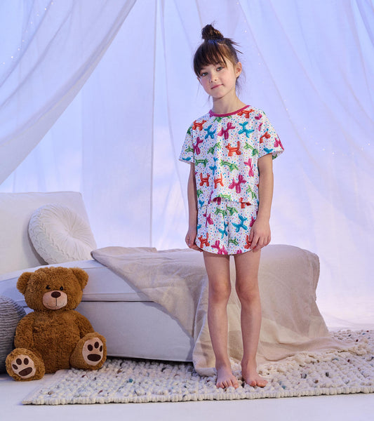 Girl wearing white short pajamas with multicolored balloon animal print and pink neckline