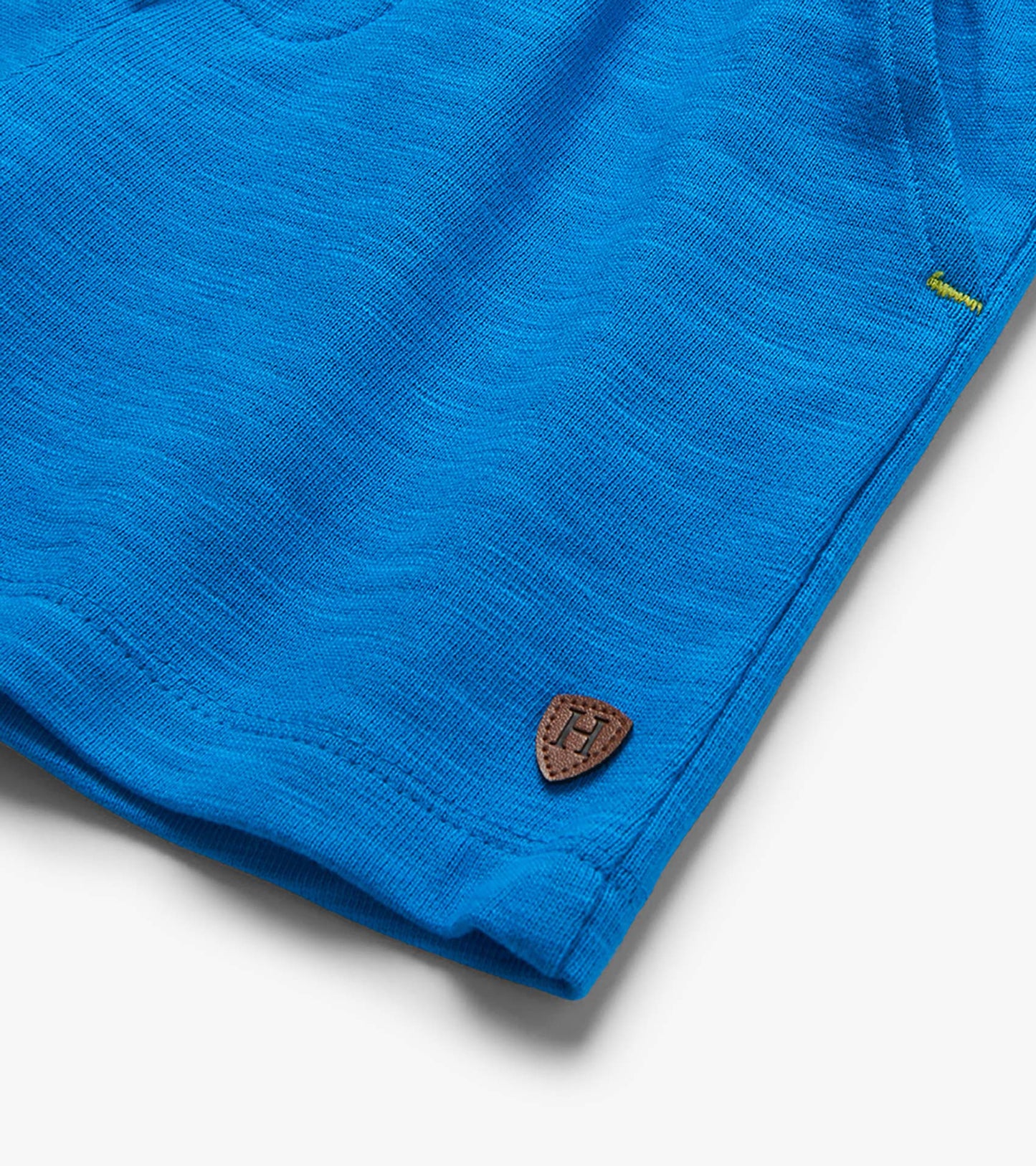 Close-up of bright blue knit shorts hem with stitched logo patch and small embroidered detail