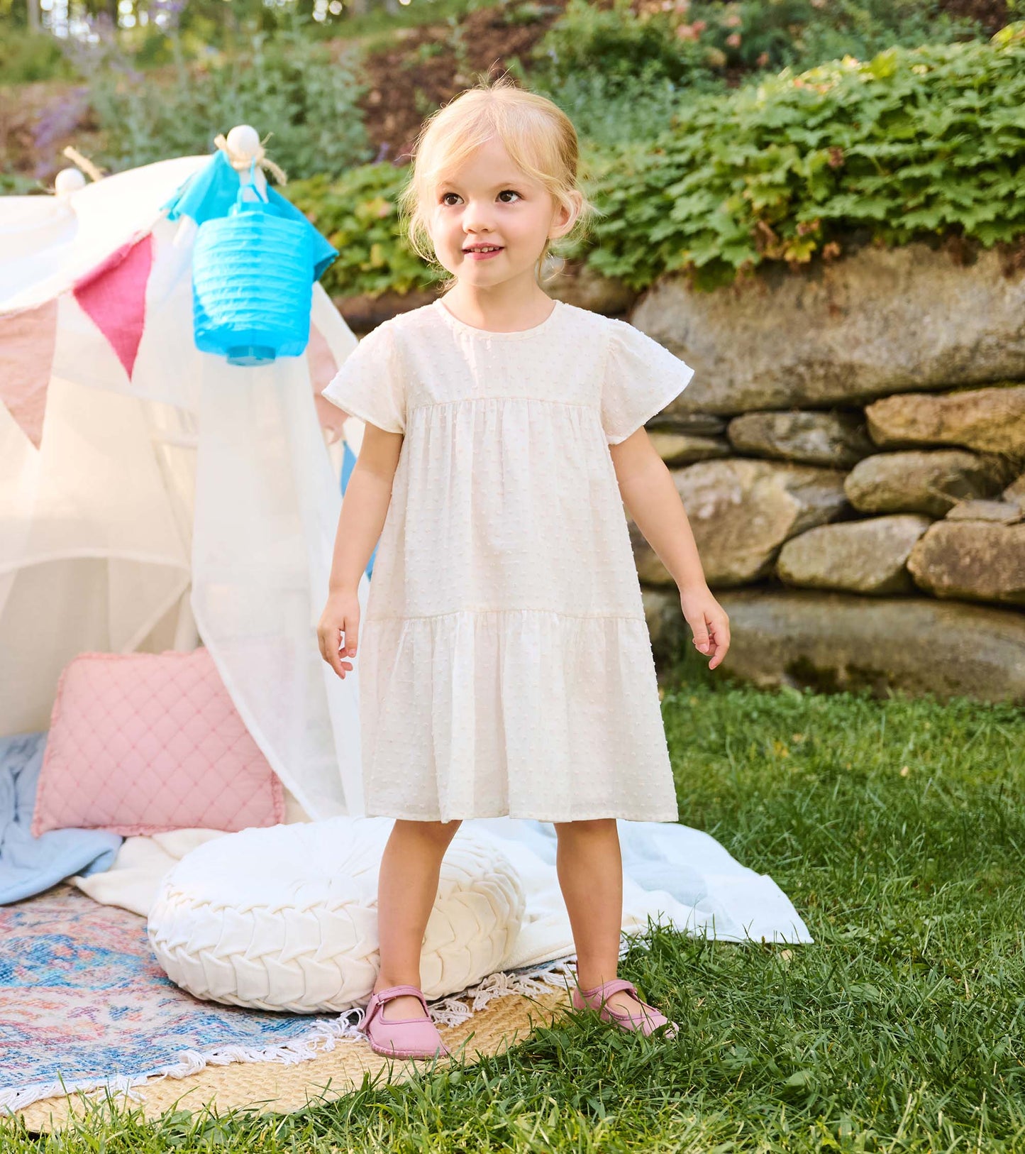 Toddler girl wearing a pearl white Swiss dot dress with puff sleeves and tiered skirt outdoors