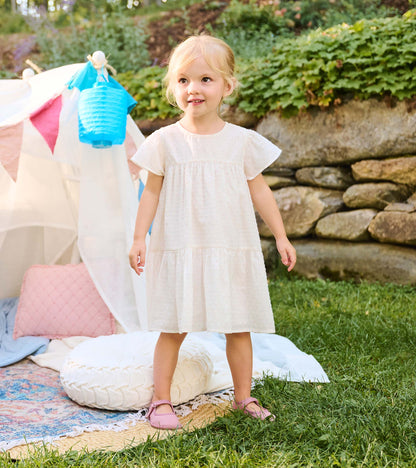 Toddler girl wearing a pearl white Swiss dot dress with puff sleeves and tiered skirt outdoors