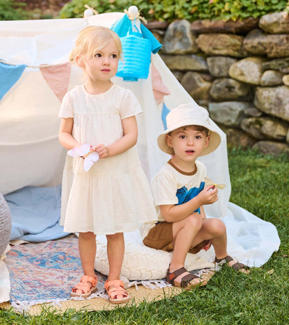 Toddler in pearl Swiss dot dress standing outdoors beside another child