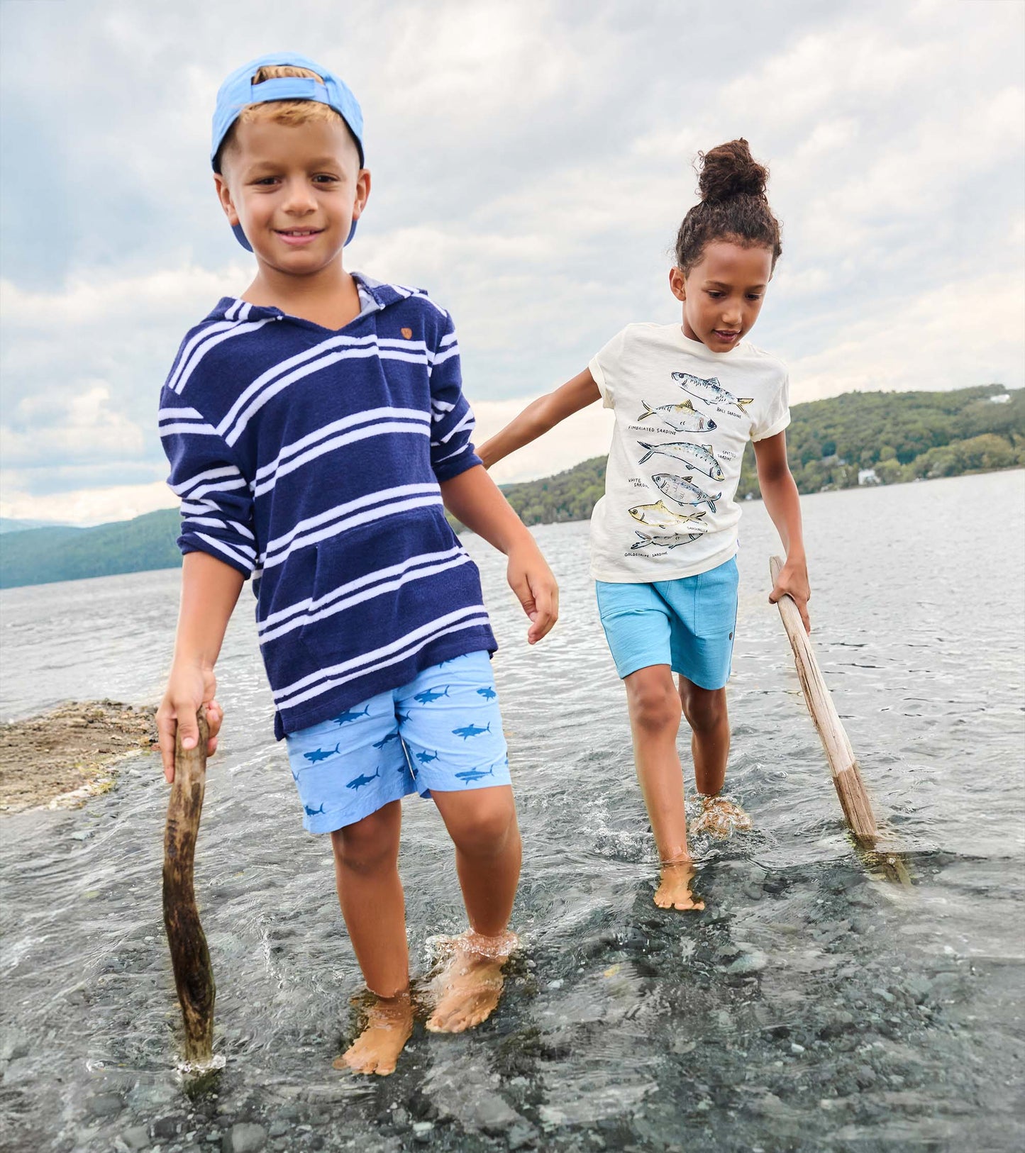 Boy wearing navy striped hooded long-sleeve cover-up with light blue shorts, standing in shallow water