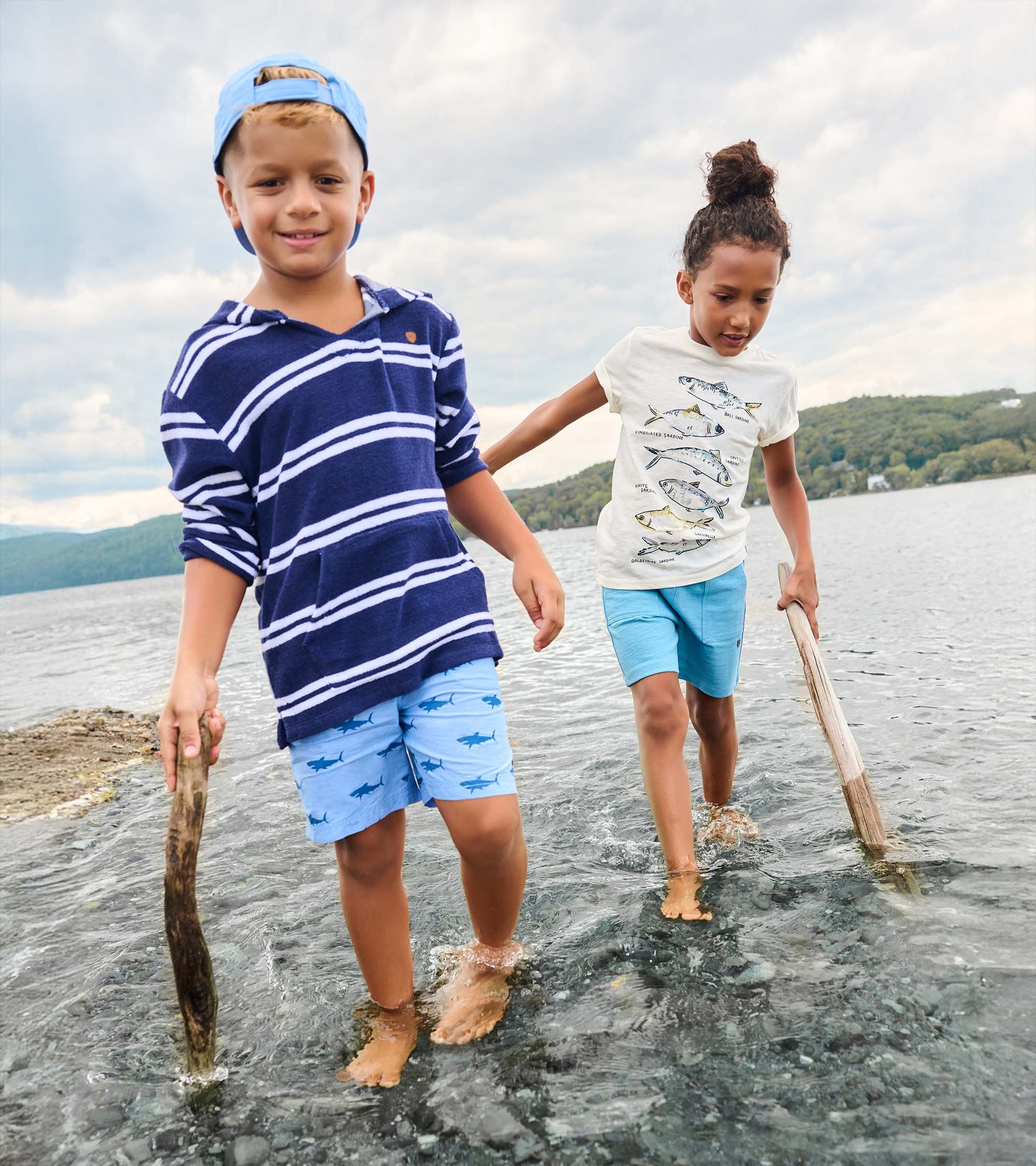 Boy wearing navy striped hooded long-sleeve cover-up with light blue shorts, standing in shallow water