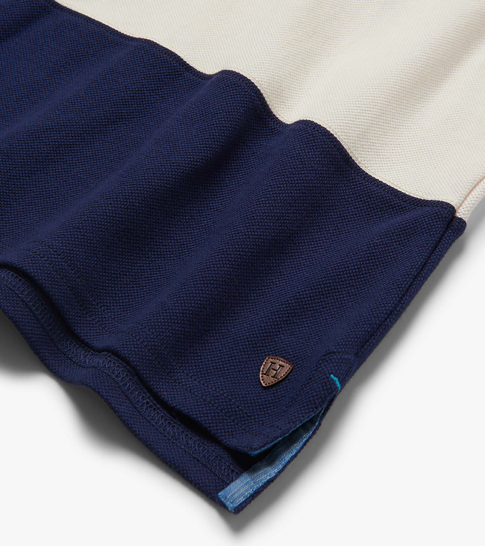 Folded navy and white color block polo shirt with textured knit fabric and small chest logo patch