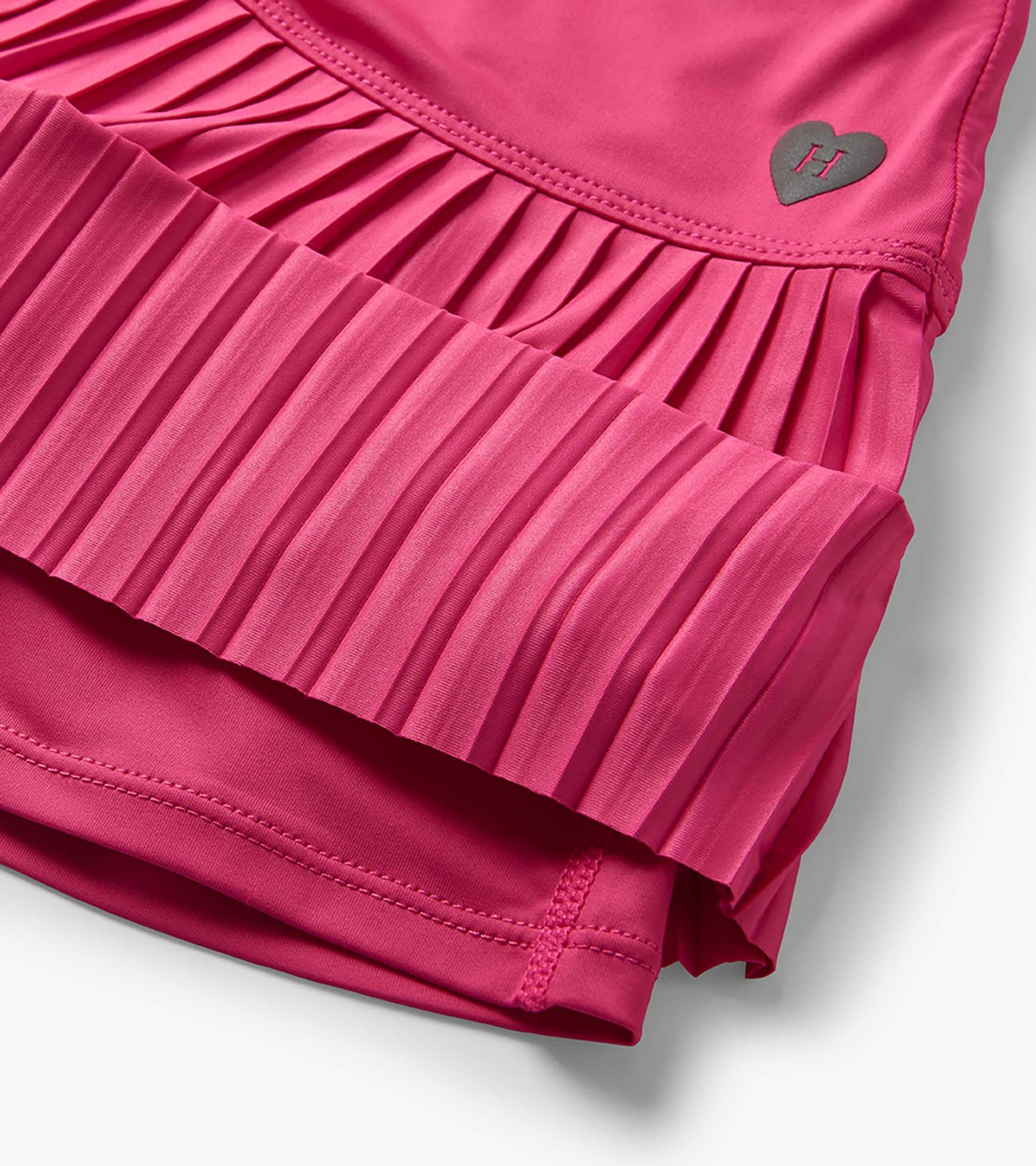 Pink girls sporty skort with pleated overlay and heart logo detail, close-up view