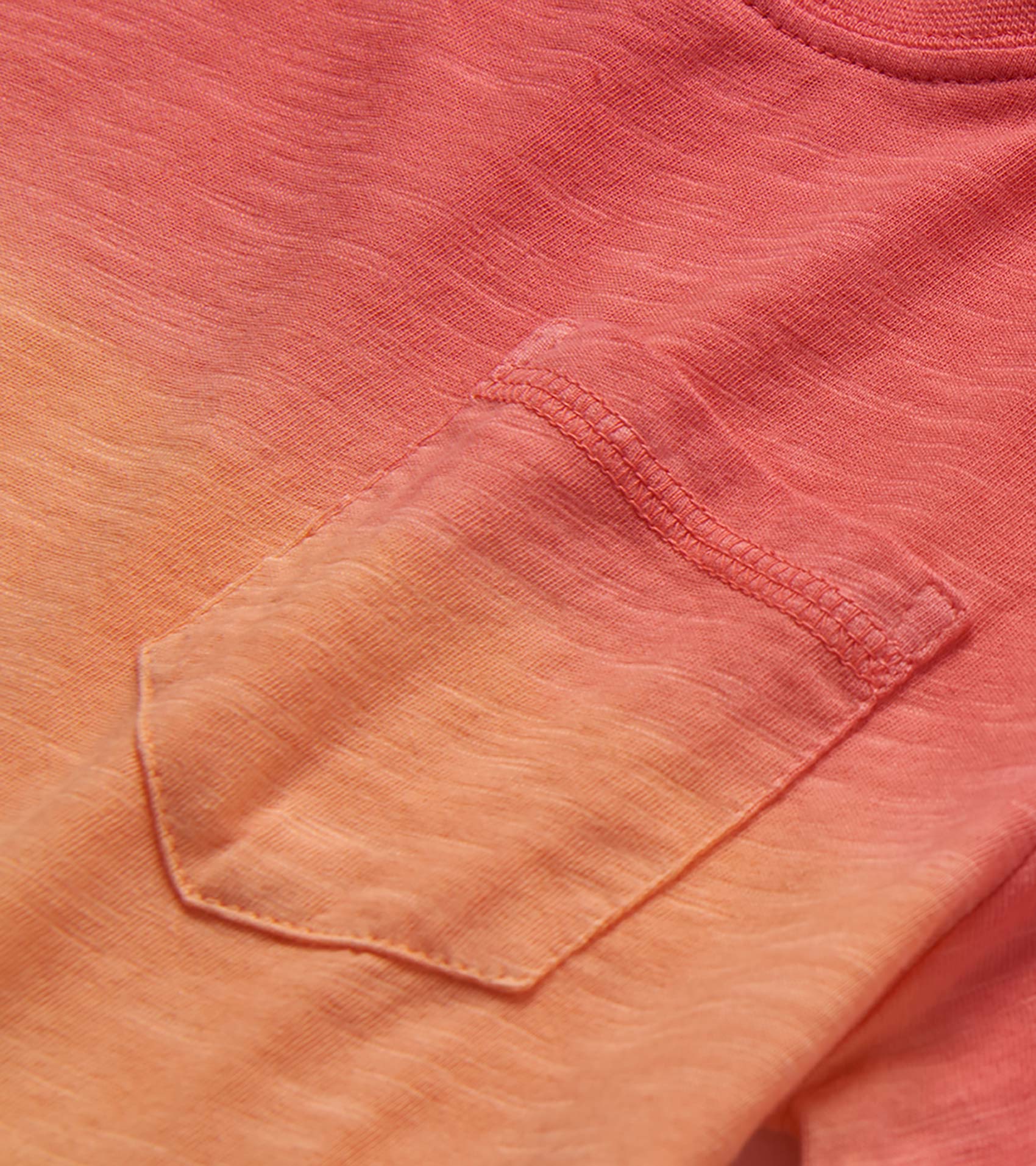 Close-up of a coral-to-peach gradient crew neck T-shirt with chest pocket and stitched details