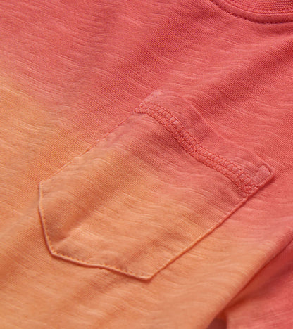 Close-up of a coral-to-peach gradient crew neck T-shirt with chest pocket and stitched details