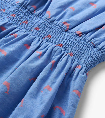Close-up of blue dress smocked waistband with pink dolphin print and gathered skirt detail