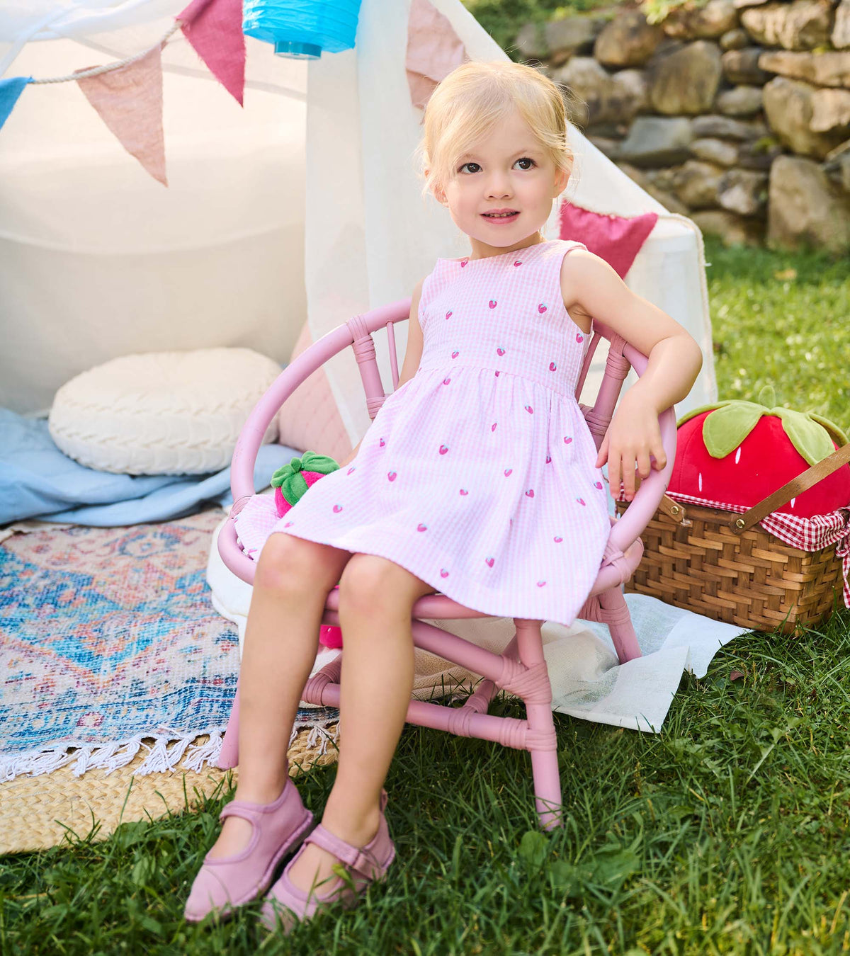 Toddler seated in pink chair wearing pink gingham dress with small strawberry pattern