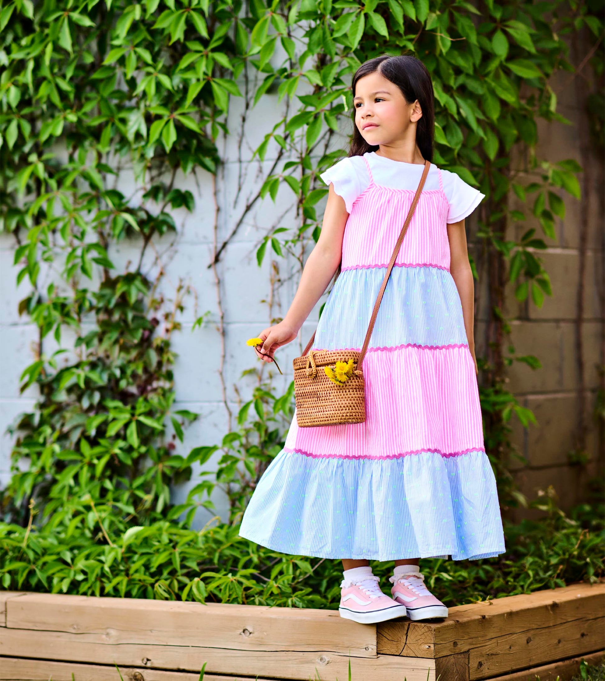 Girl wearing a tiered midi dress with pink and blue striped panels and pink trim, standing outdoors