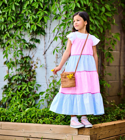 Girl wearing a tiered midi dress with pink and blue striped panels and pink trim, standing outdoors