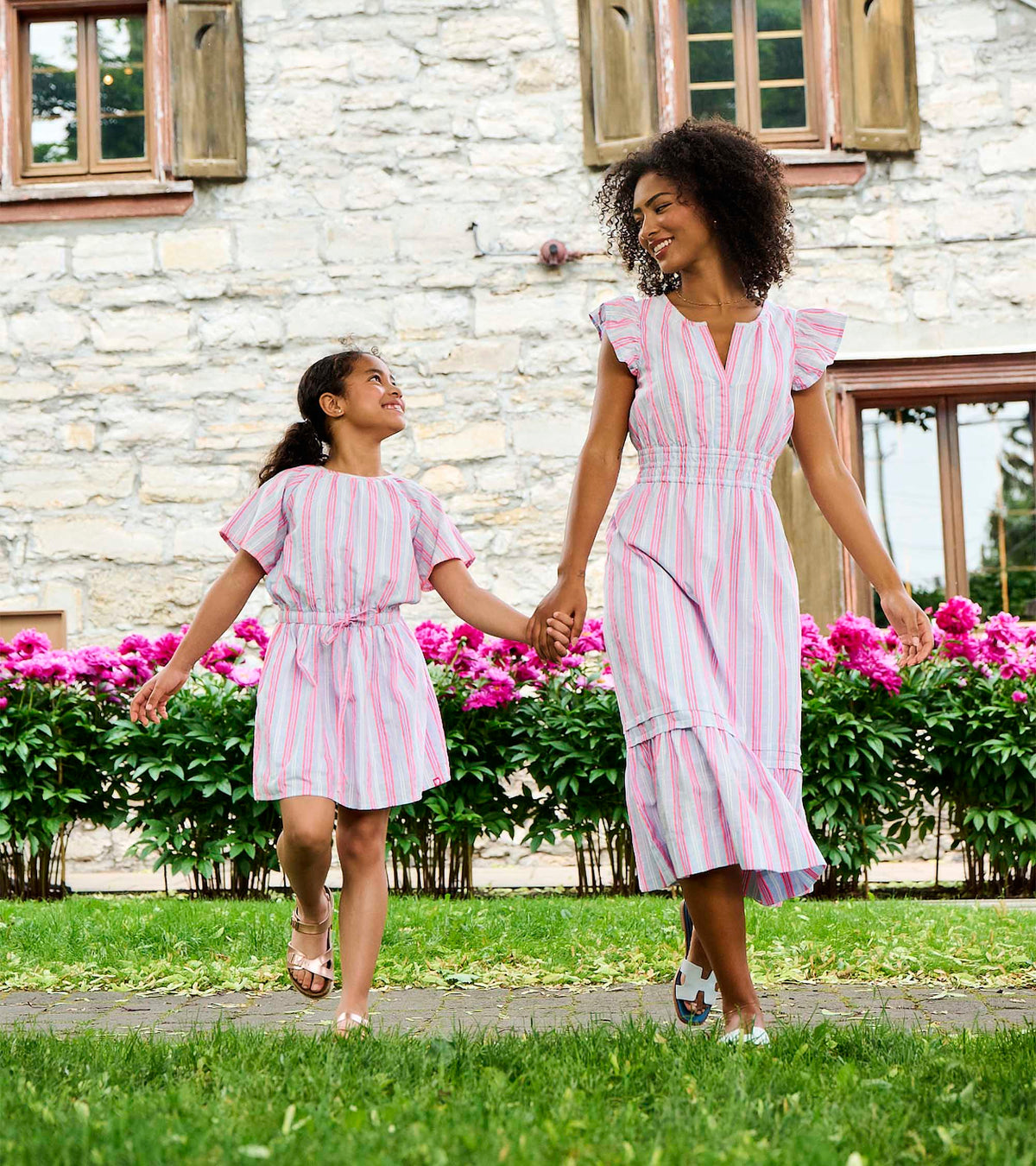 Mother and daughter wearing pink and blue striped woven dresses outdoors, holding hands
