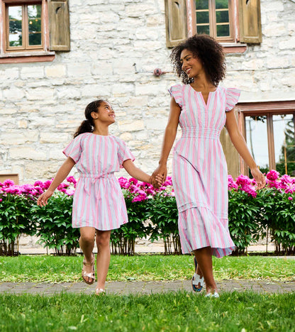 Mother and daughter wearing pink and blue striped woven dresses outdoors, holding hands