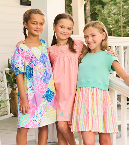 Three girls wearing colorful summer dresses, including a patchwork print dress, a pink dress, and a mint top with striped sk…
