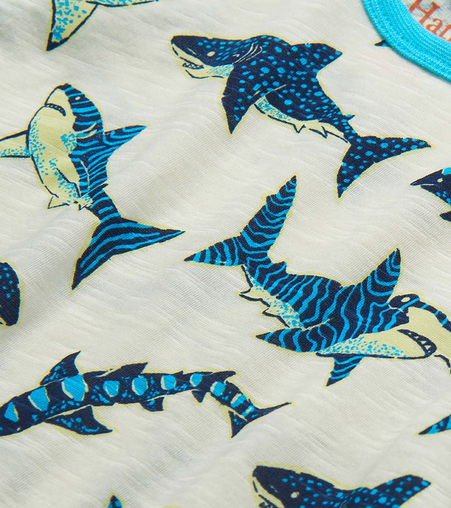 Close-up of white fabric with blue and teal shark print on a boys' raglan T-shirt