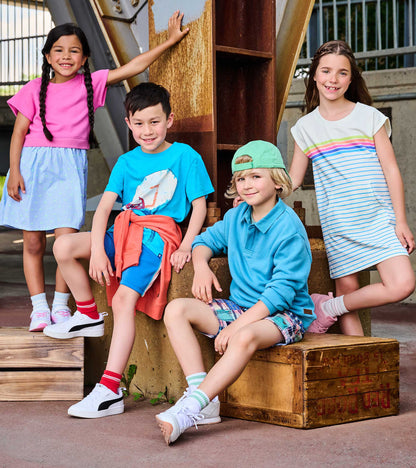 Girl in white dress with rainbow stripes, short sleeves, and knee-length hem, standing outdoors