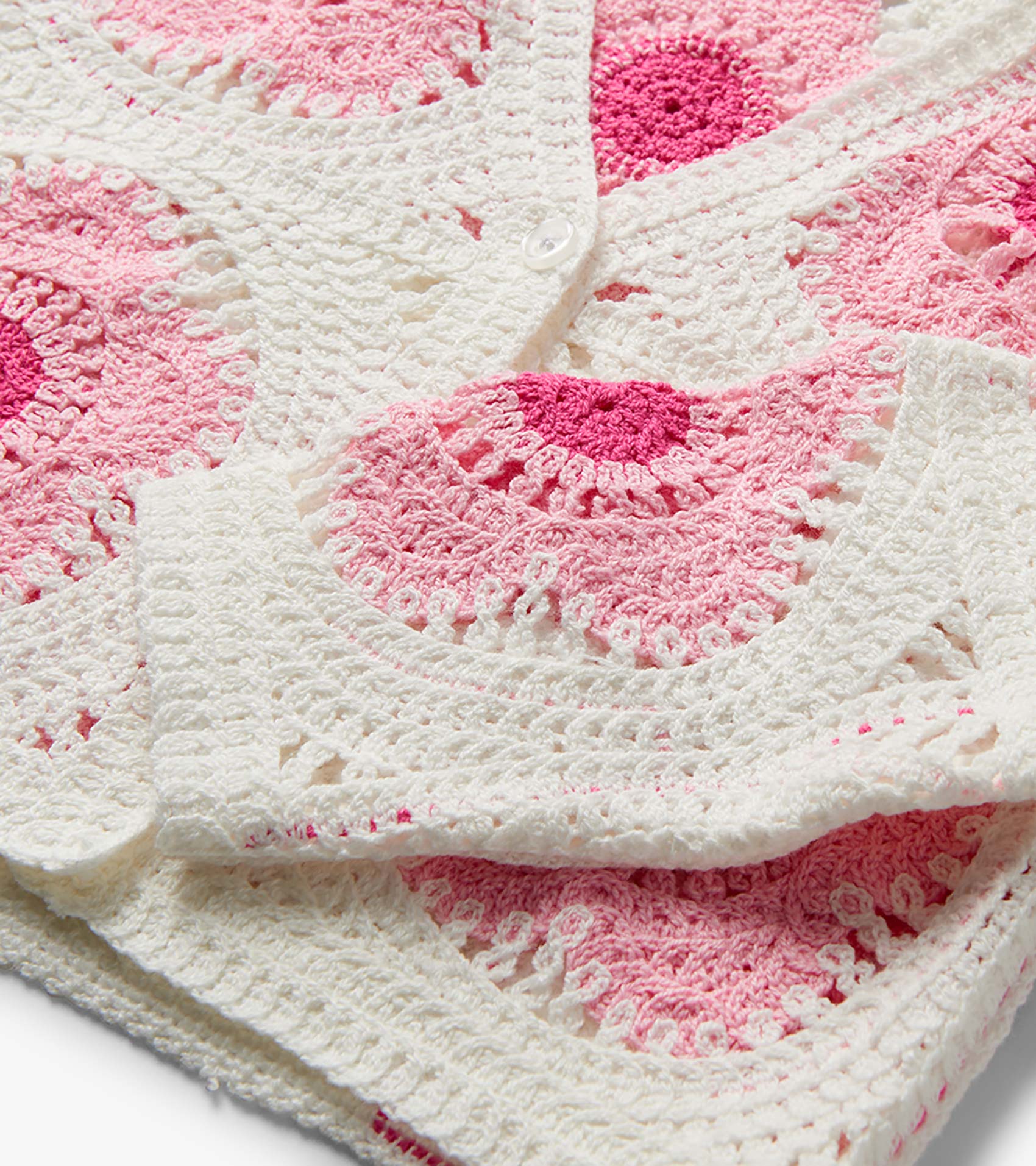 Close-up of a pink and cream crochet cardigan with floral pattern and white button closure