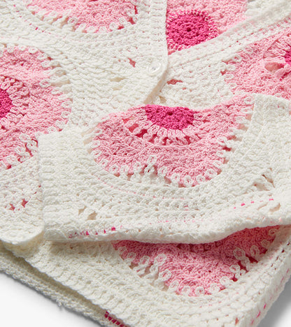 Close-up of a pink and cream crochet cardigan with floral pattern and white button closure