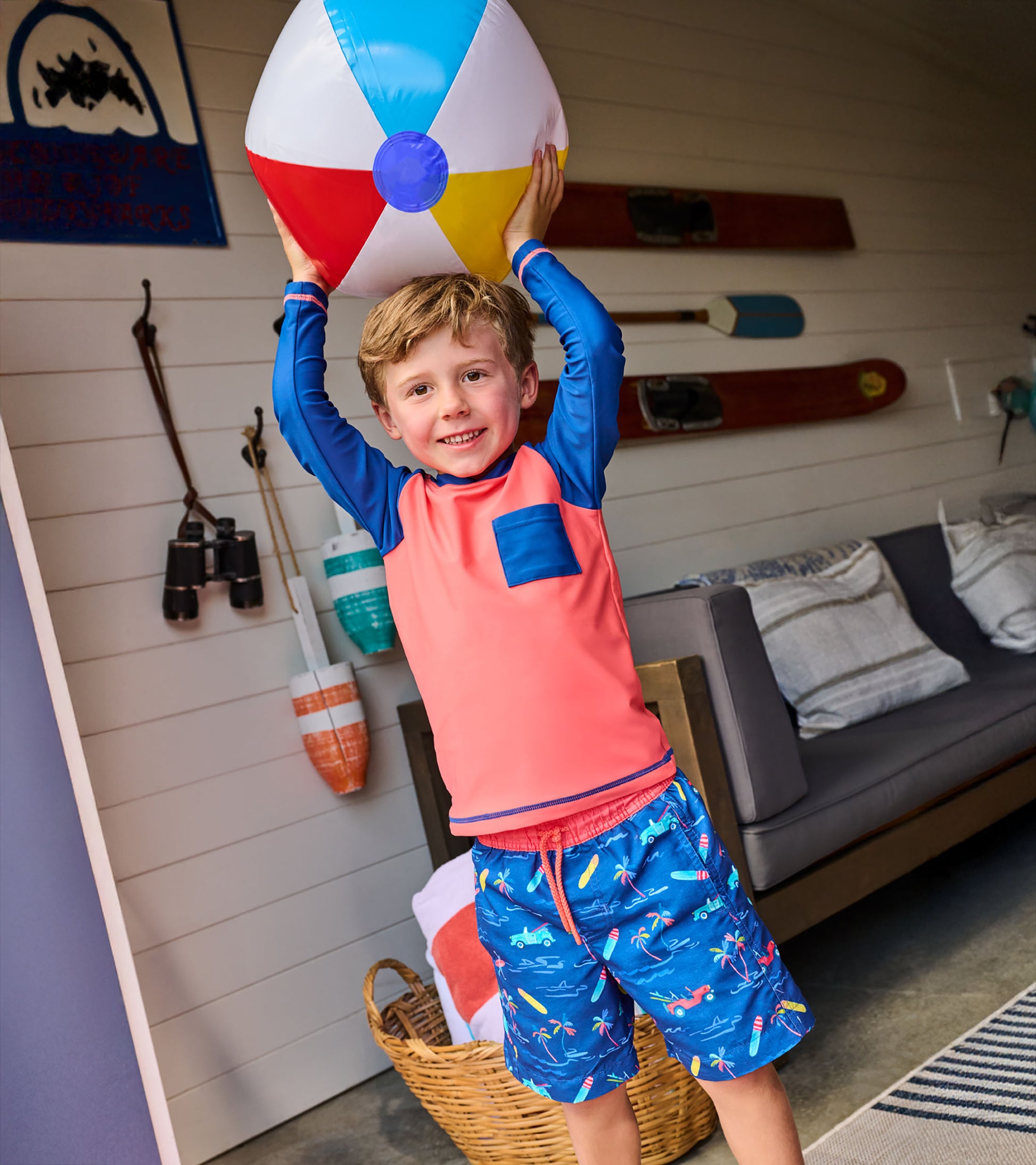 Boy wearing coral and navy long-sleeve rashguard with chest pocket, holding a beach ball indoors