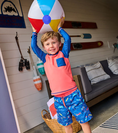 Boy wearing coral and navy long-sleeve rashguard with chest pocket, holding a beach ball indoors