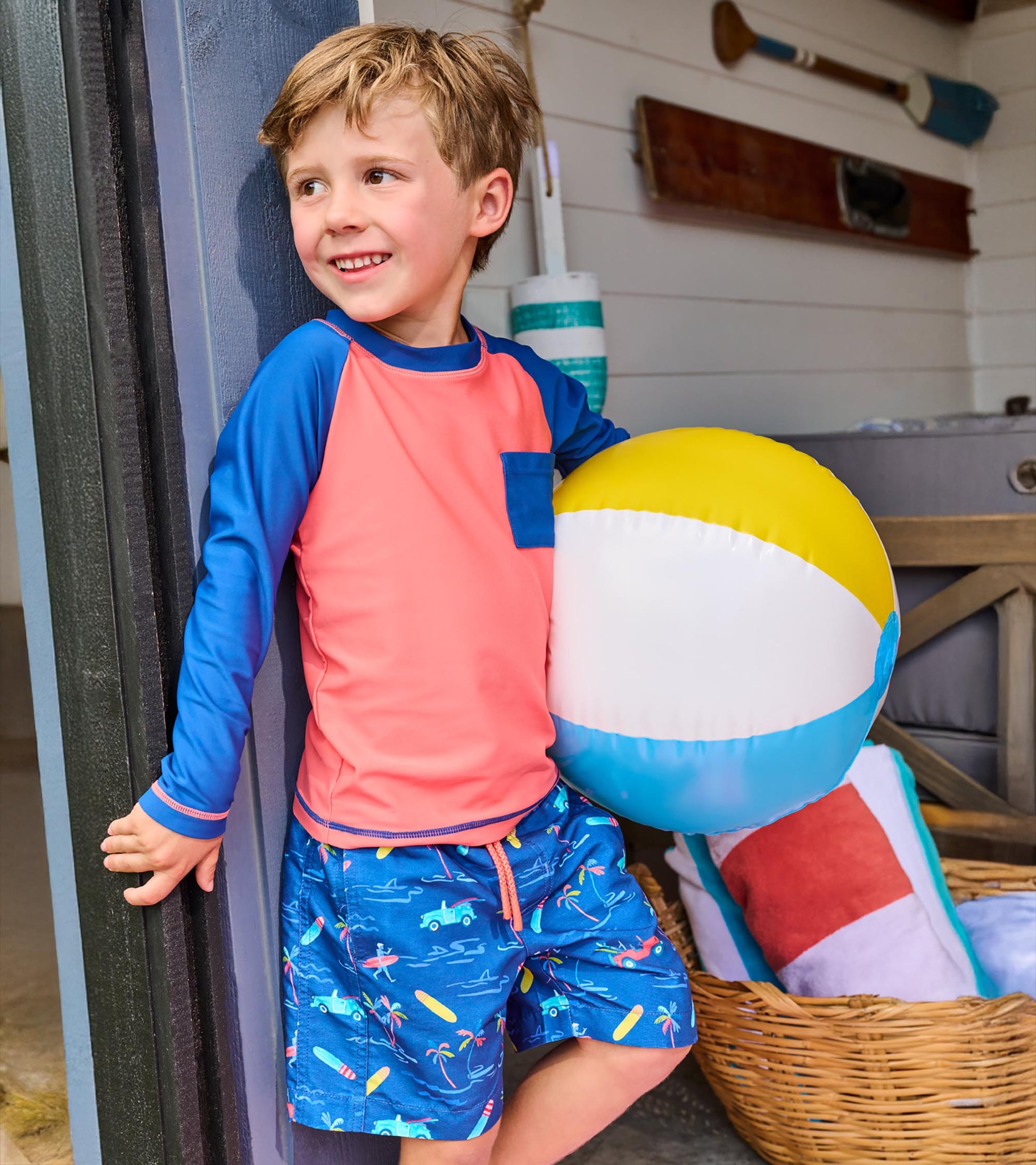 Boy wearing coral and navy long-sleeve rashguard with blue sleeves and chest pocket, front view