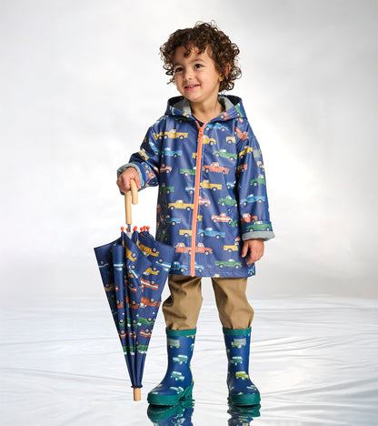 Boy wearing a navy zip-up raincoat with colorful truck print and coral zipper, holding a matching umbrella
