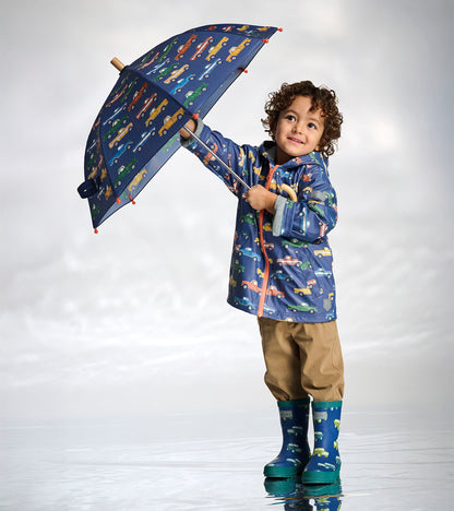 Boy wearing a navy zip-up raincoat with colorful truck print and matching rain boots, holding an umbrella