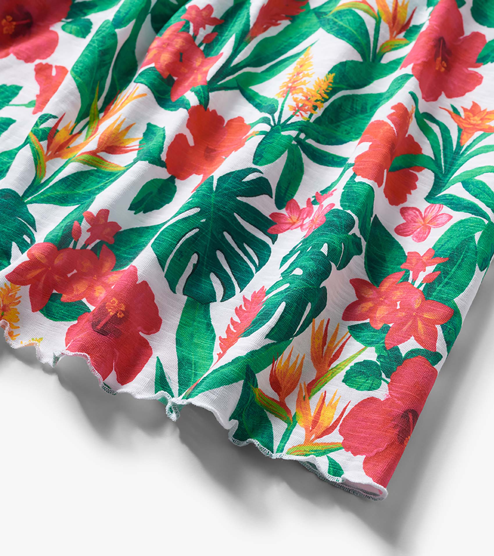 White dress fabric with green leaves and pink-orange tropical flowers, close-up of hemline