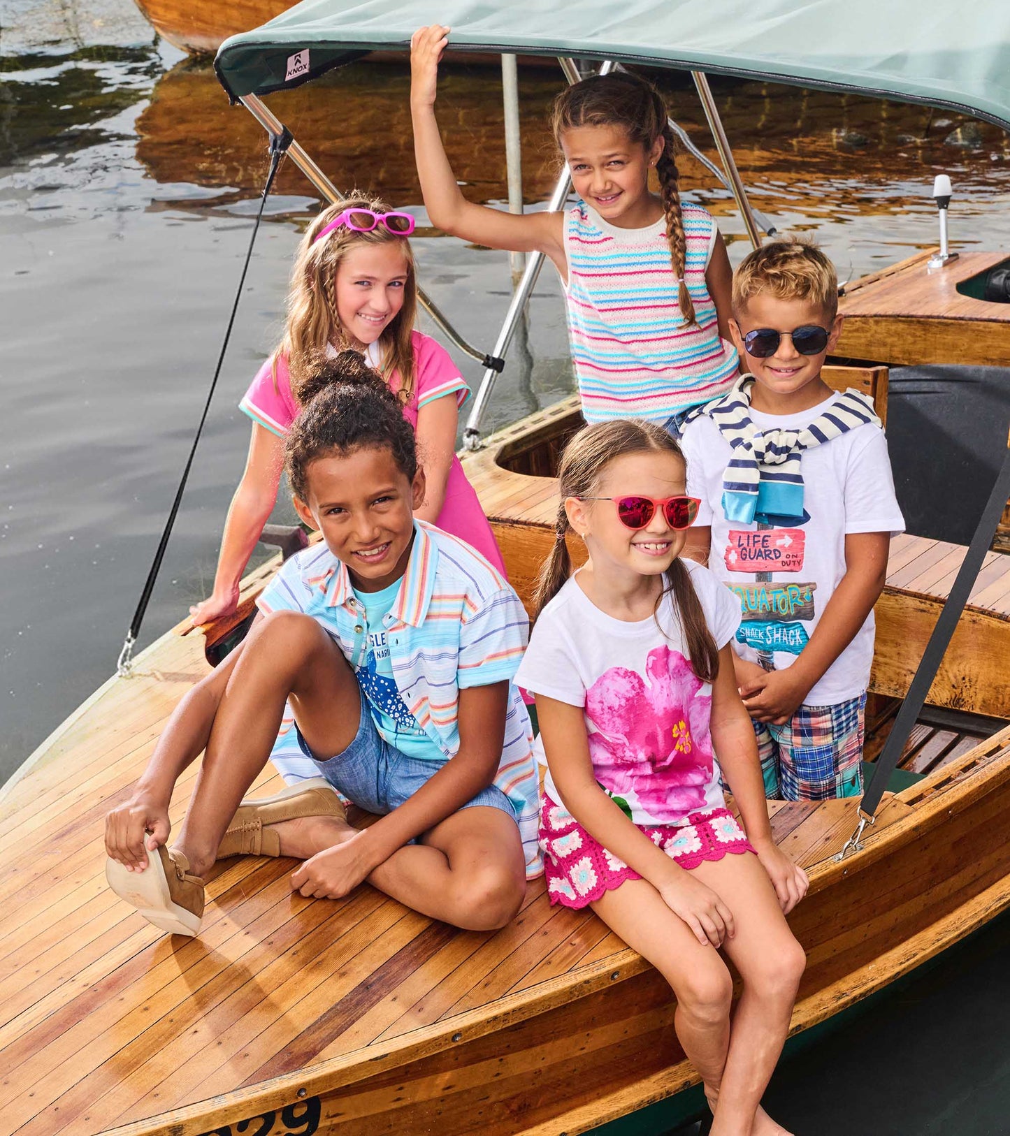 White boys graphic tee with colorful beach-themed print, shown on a child standing on a boat