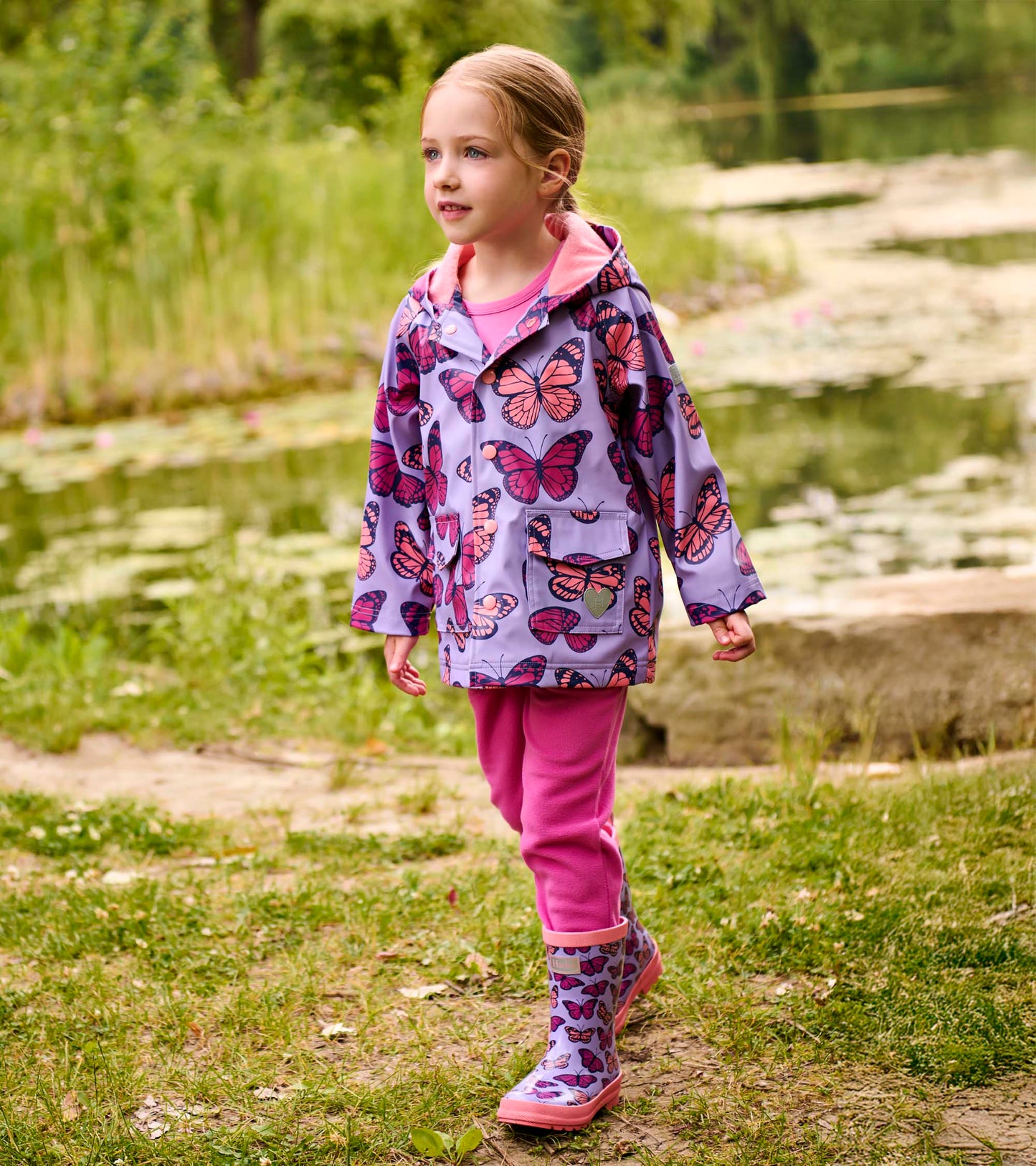 Girl wearing a lavender butterfly-print hooded raincoat with pink lining and buttons, front view