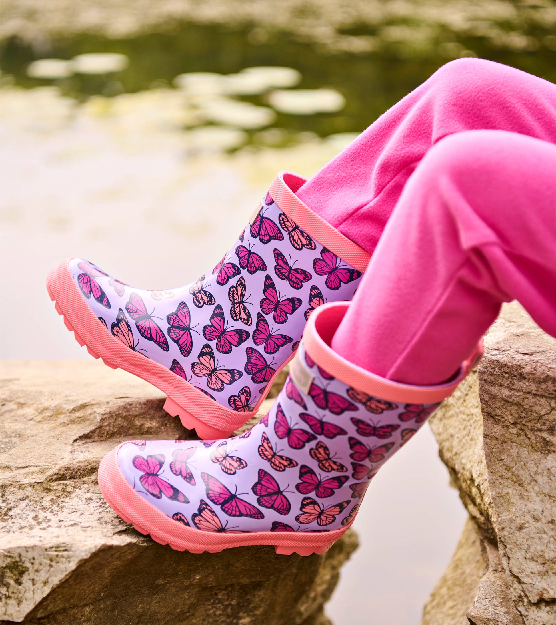 Lavender kids rain boots with pink butterfly print and pink trim, shown on feet outdoors