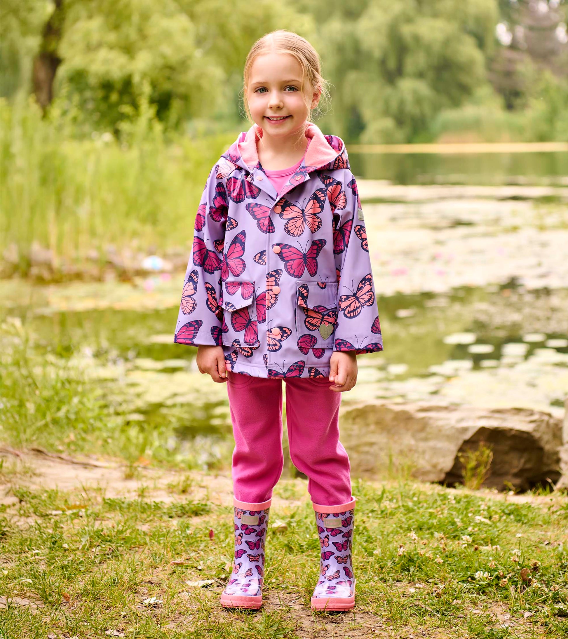 Girls lavender butterfly print rain boots with pink soles, front view on a child outdoors
