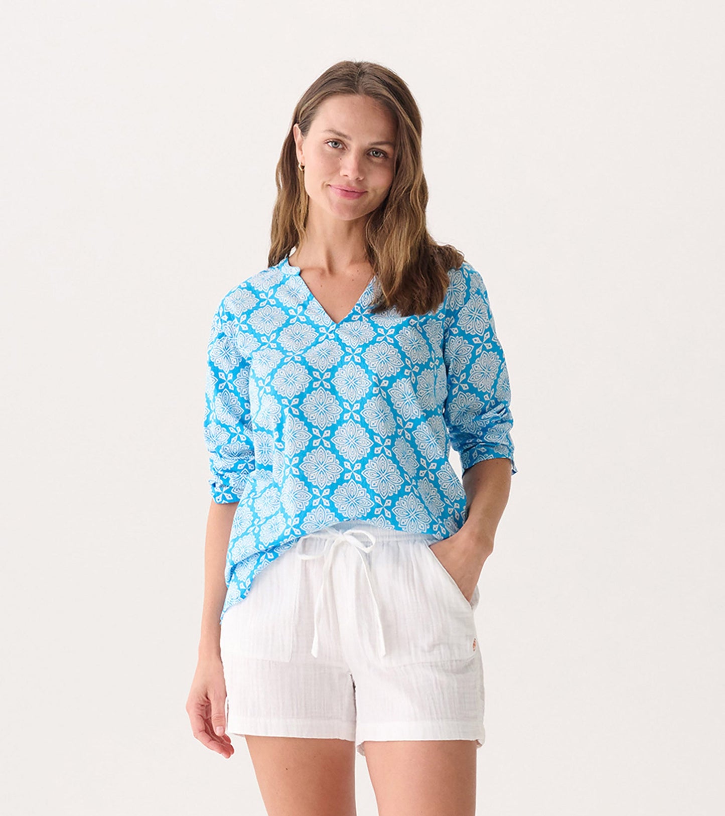 Blue tunic with white floral pattern, featuring a V-neck and long sleeves, paired with white shorts.