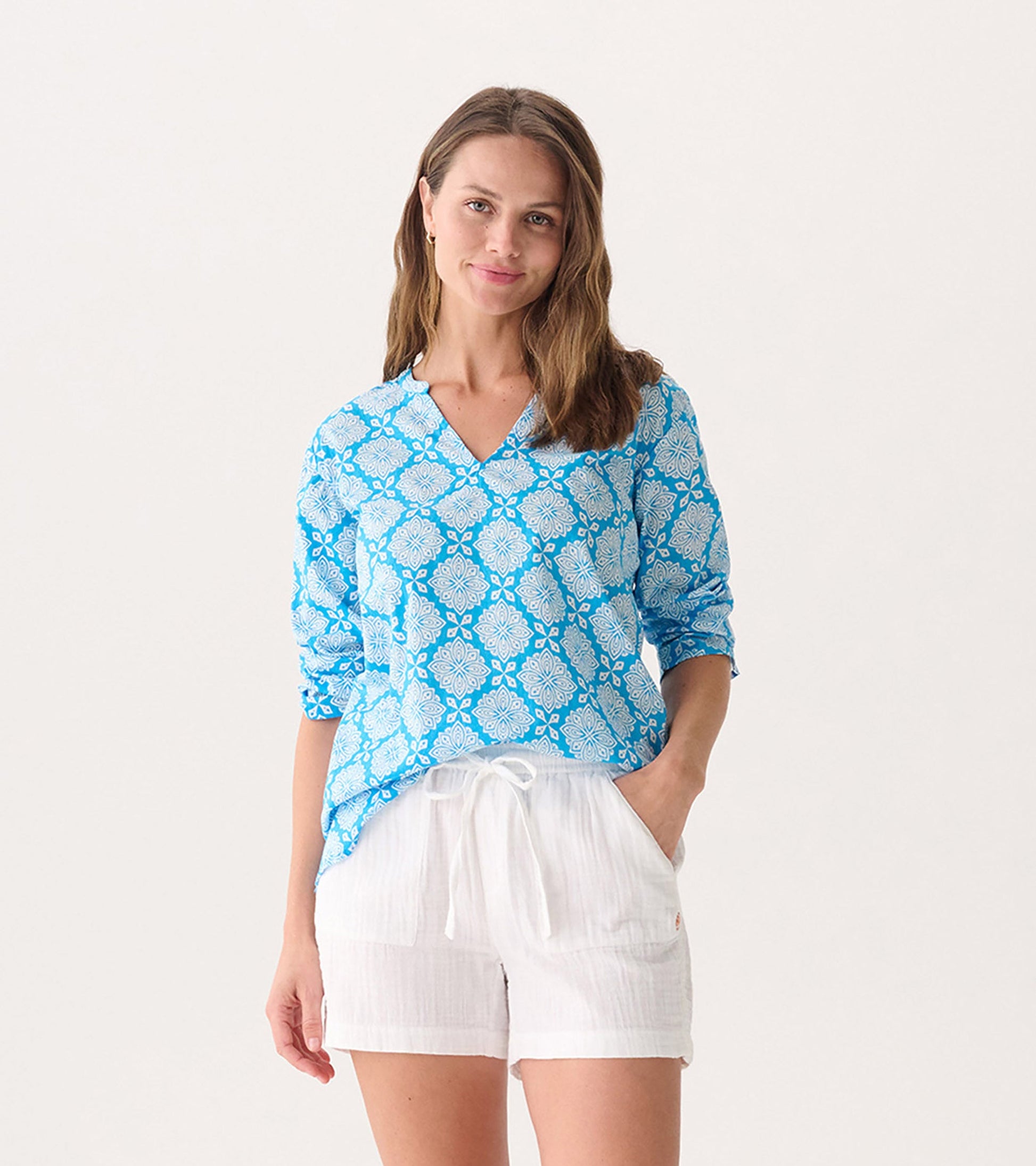 Blue tunic with white floral pattern, featuring a V-neck and long sleeves, paired with white shorts.