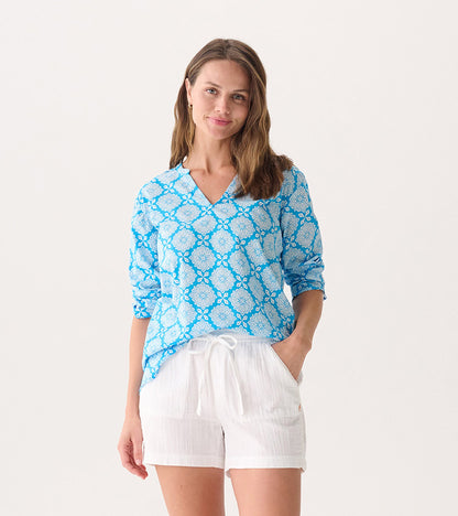 Blue tunic with white floral pattern, featuring a V-neck and long sleeves, paired with white shorts.
