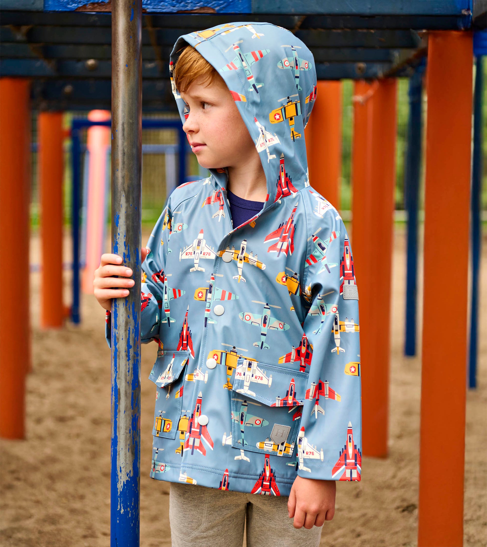 Blue hooded boys raincoat with colorful airplane print, front view, worn by a child outdoors